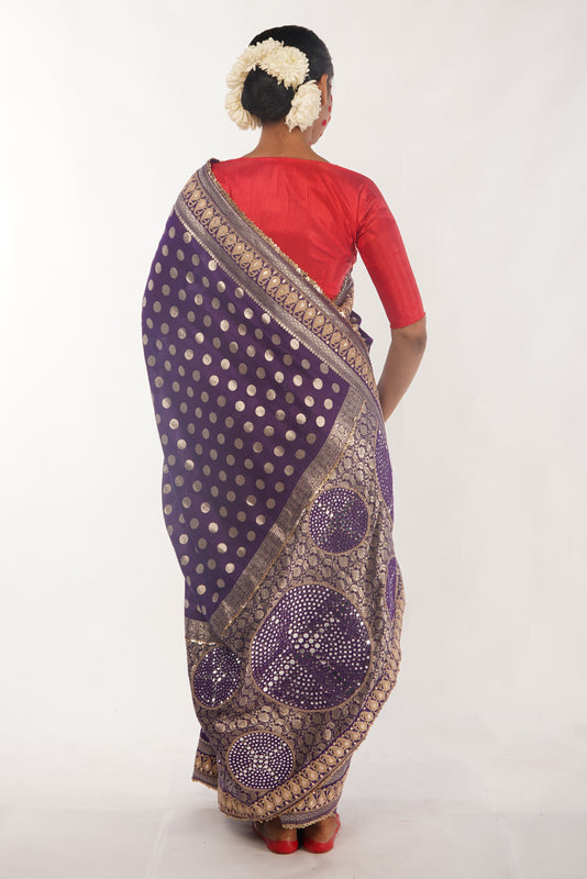 Woman wearing a purple benarsi silk saree with gold patterns on a white background