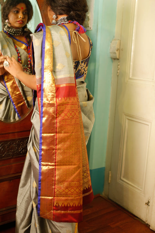 Woman wearing a  traditional beautiful handwoven English grey and antique gold Kanjiveeram silk saree  with a mirror reflection in the background