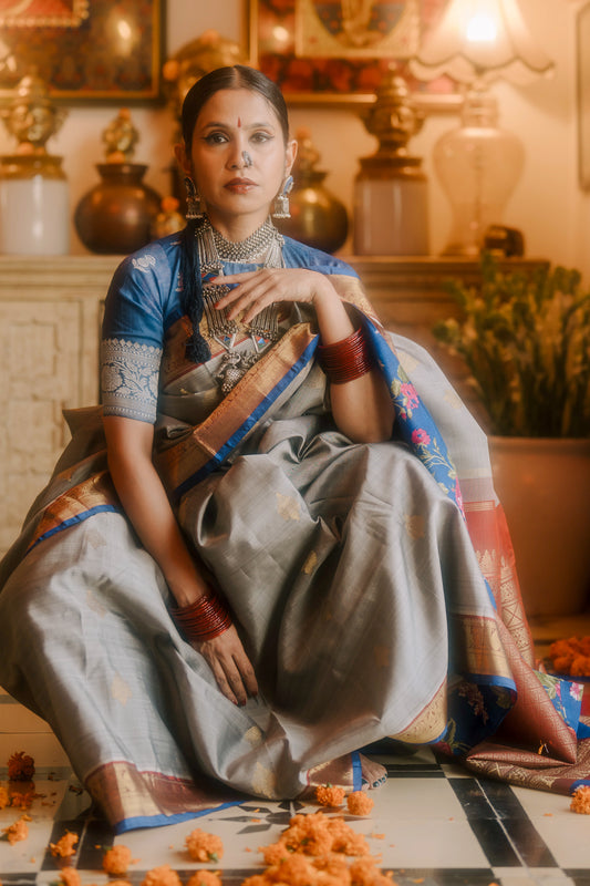 Woman in traditional beautiful handwoven English grey and antique gold Kanjivaram silk saree sitting in a decorated indoor setting