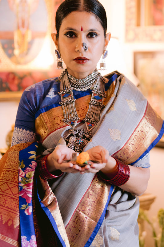 Woman in traditional beautiful handwoven English grey and antique gold Kanjiveeram silk saree holding a fruit with a blurred background