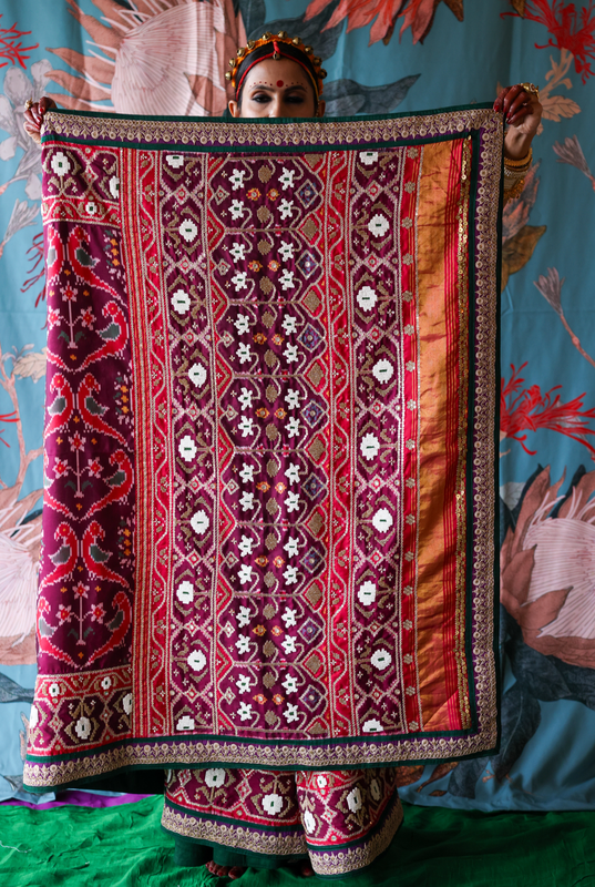 Traditional hand embroidery and hand woven patola silk saree held by a person against a colorful background