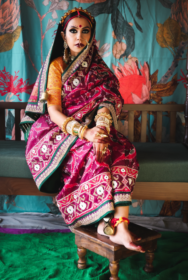 Person wearing a traditional pink patola silk saree with gold patterns sitting on a bench.
