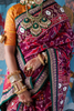 Person wearing a colorful hand embroidered patola silk saree with intricate patterns and jewelry, holding a phone.