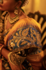 Close-up of a person wearing traditional jewelry and a kanjiveeram silk saree with intricate patterns.