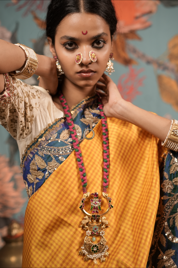 Woman in traditional attire with jewelry, including a large necklace, in an indoor setting.