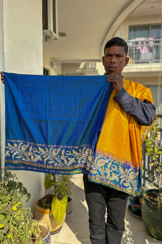 Person holding a blue and yellow patterned kanjiveeram silk saree outdoors.