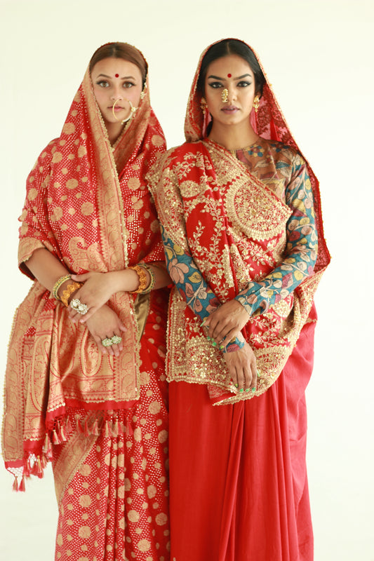 Two women wearing red embroidered wedding sarees designed by Ayush Kejriwal.